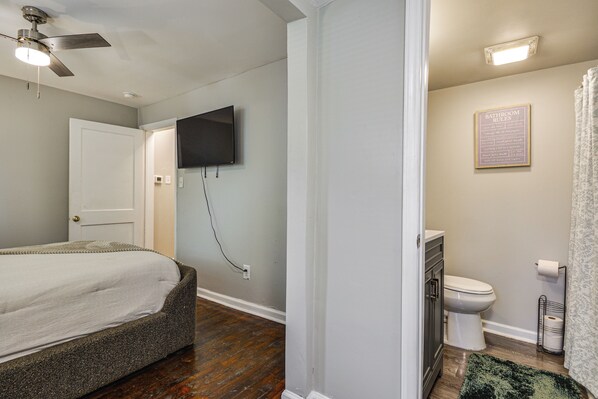 A bedroom with a bed, a ceiling fan, a mounted TV, and a bathroom with a toilet, shower curtain, and a towel rack. - Updated Jamestown Home - 5 Mi to Hpu! (Jamestown)