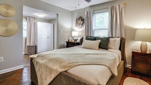 Quarto com cama, mesa de cabeceira, abajur, ventoinha no teto e janela com cortinas.