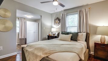 A bedroom with a bed, a nightstand, a lamp, a ceiling fan, and a window with curtains.