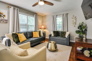 Una sala de estar con un sofá de cuero negro, un sofá gris y un sillón color beige. Hay una lámpara, un jarrón decorativo y una mesita con un libro.