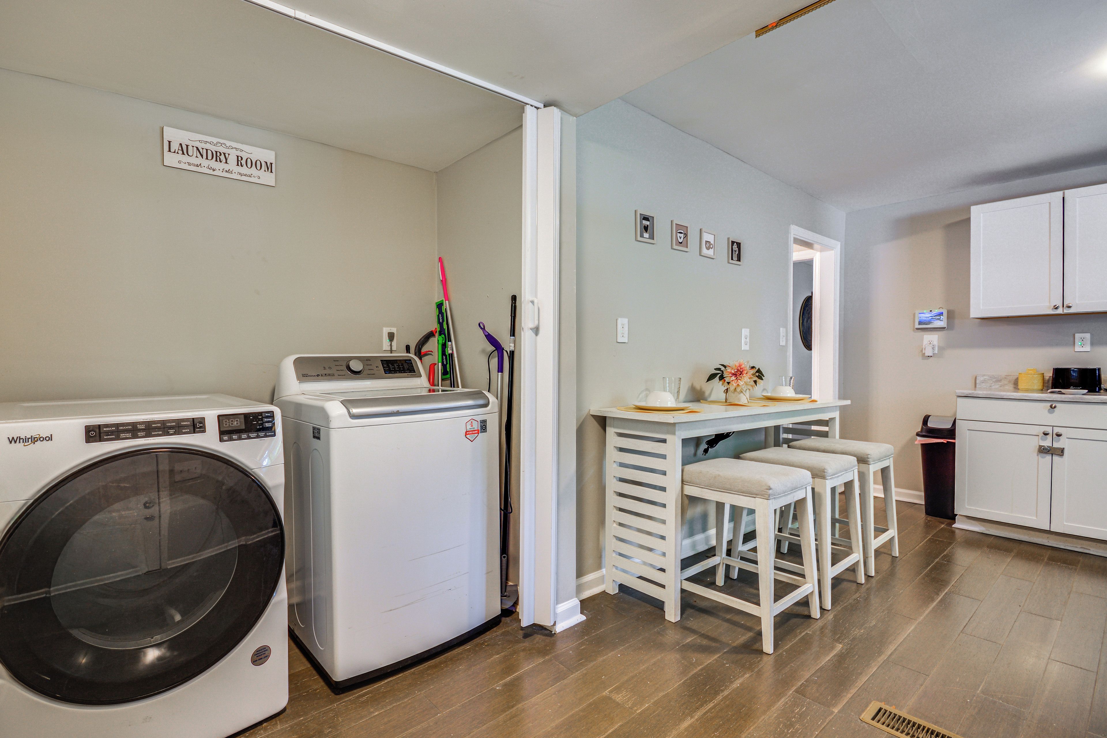 Un lavadero con lavadora y secadora Whirlpool, una mesita con taburetes y un cartel que indica servicios de lavandería.