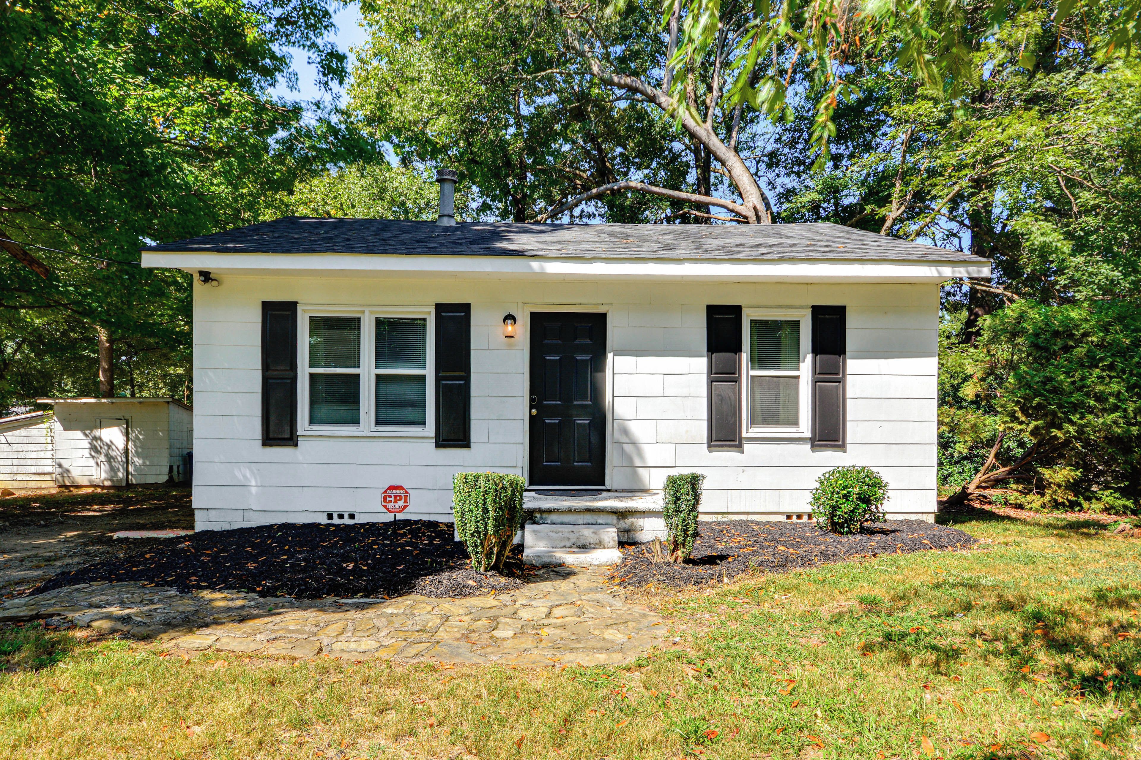 A single-story house with a black front door, white siding, and a small front yard with a stone pathway leading to the entrance.