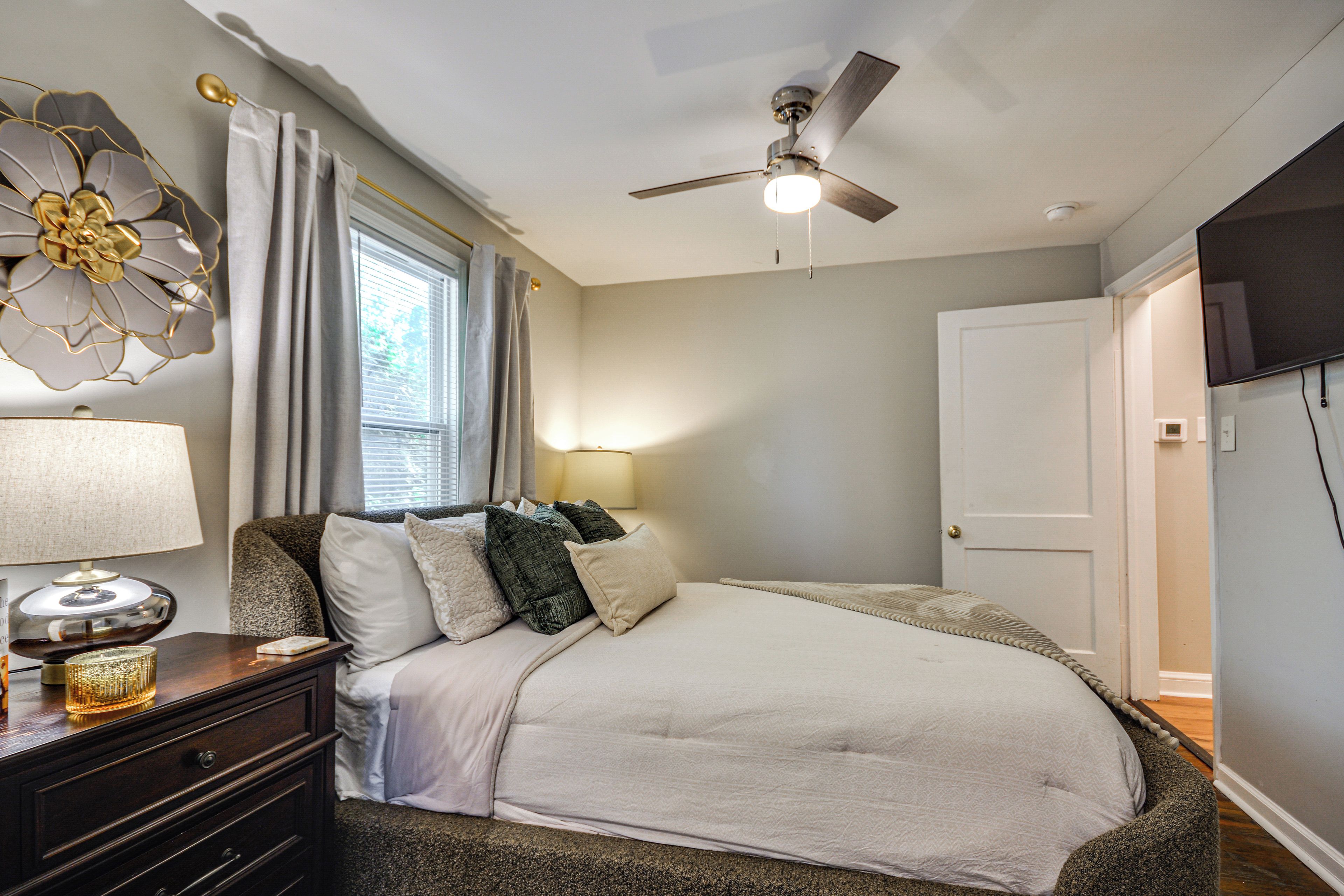 A bedroom with a bed, a nightstand, a lamp, a ceiling fan, and a door.