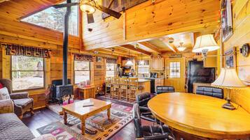 A wooden cabin interior with a dining area, kitchen, and fireplace.