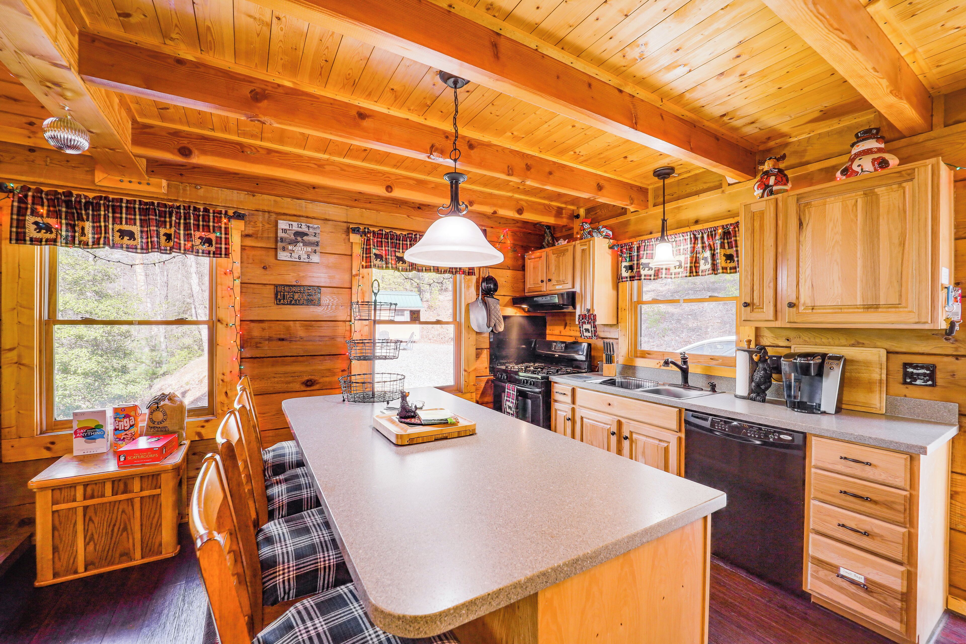 A wooden cabin interior with a kitchen, dining area, and a large window.