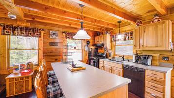 A wooden cabin interior with a kitchen, dining area, and a large window.