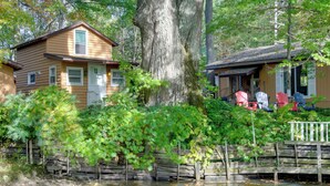 Une cabane rustique dotée d’une terrasse en bois et d’un grand arbre en arrière-plan.