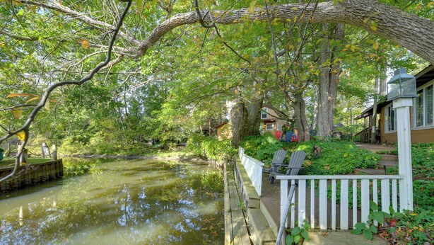 Une terrasse en bois surplombe un étang, avec une maison en arrière-plan.