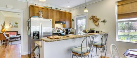 Una cocina con una isla central, taburetes de bar, armarios de madera y un refrigerador.