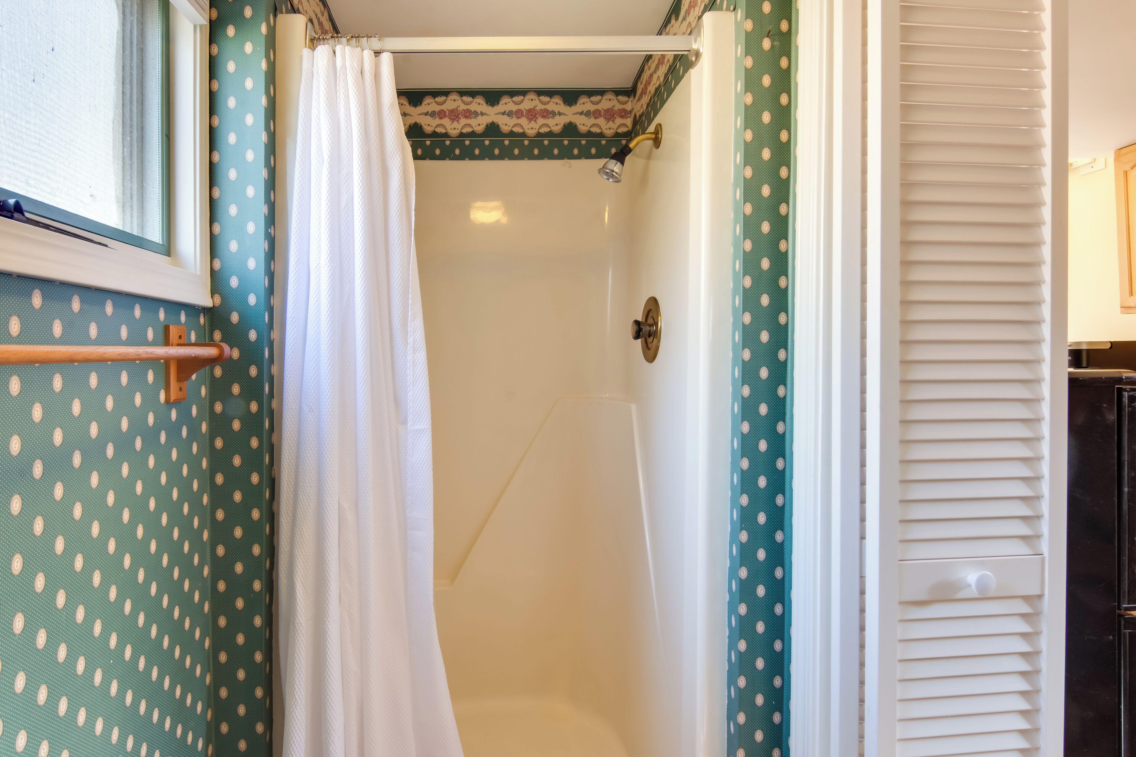 Un baño con ducha, una ventana y una puerta con perchero para toallas.