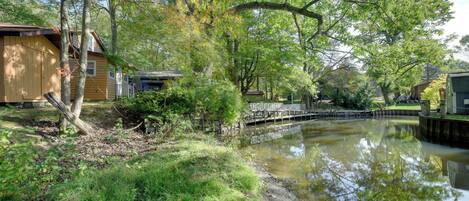 A serene riverside setting with a wooden dock, a small bridge, and a building with a sloped roof.