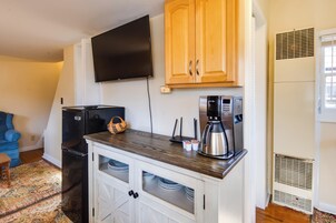 Una cocina compacta con refrigerador integrado, cafetera y televisor de pantalla plana montado en la pared.