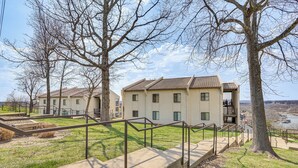 A building with multiple windows and a flat roof, surrounded by grass and trees. - Lake Ozark Condo Rental w/ View & Pool Access! (Lake Ozark)