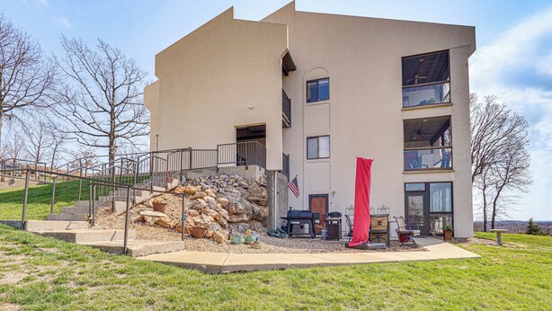 A modern two-story building with a stone facade, a flag, outdoor seating, and a red awning. - Lake Ozark Condo Rental w/ View & Pool Access! (Lake Ozark)