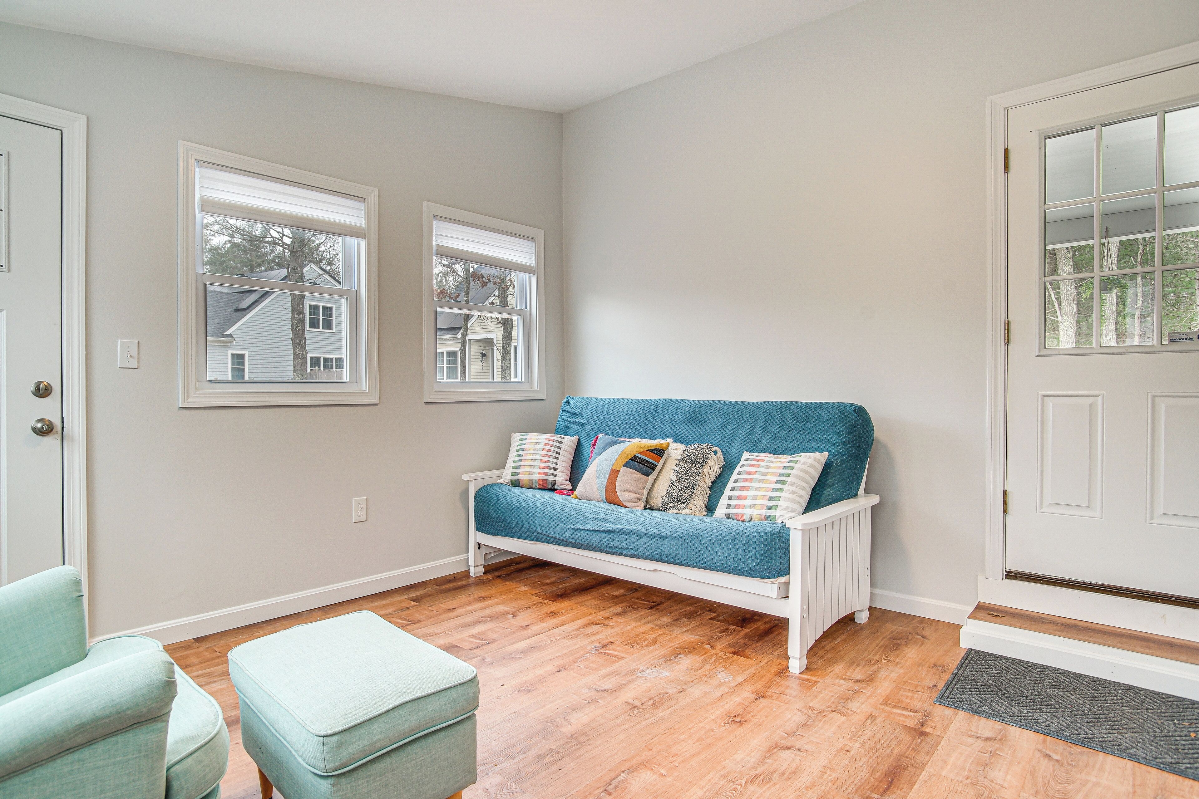 A room with a white sofa, a matching ottoman, and a window with blinds.