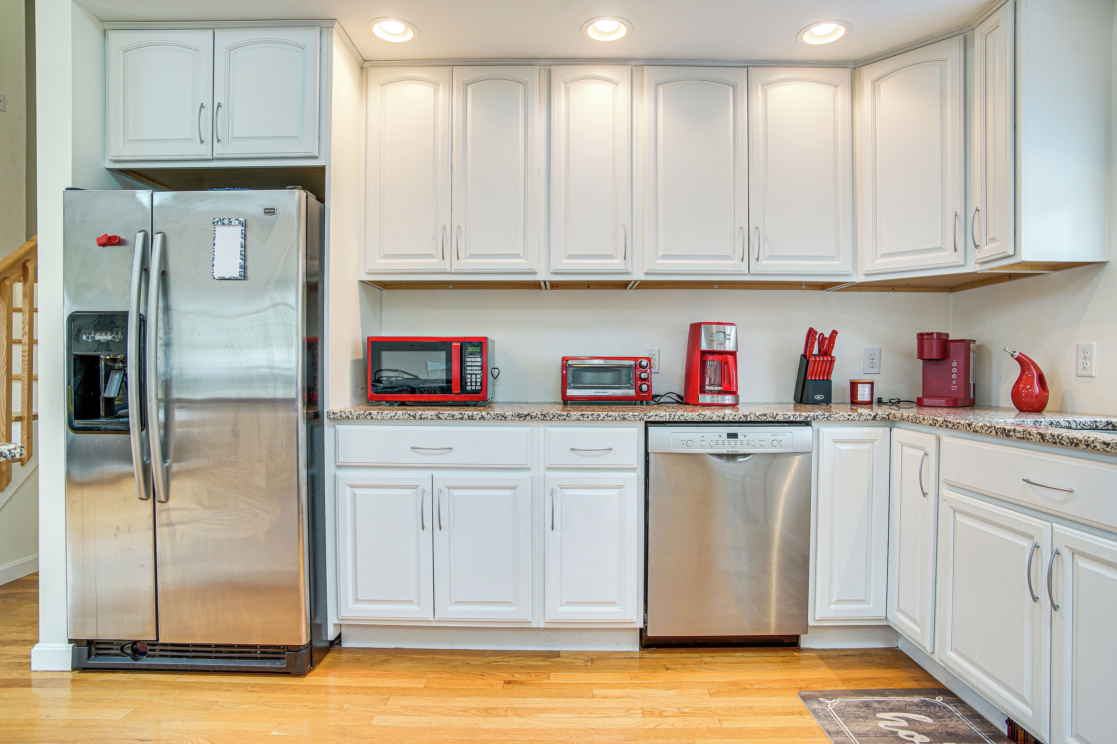 A modern kitchen with white cabinets, stainless steel appliances, and a wooden floor.