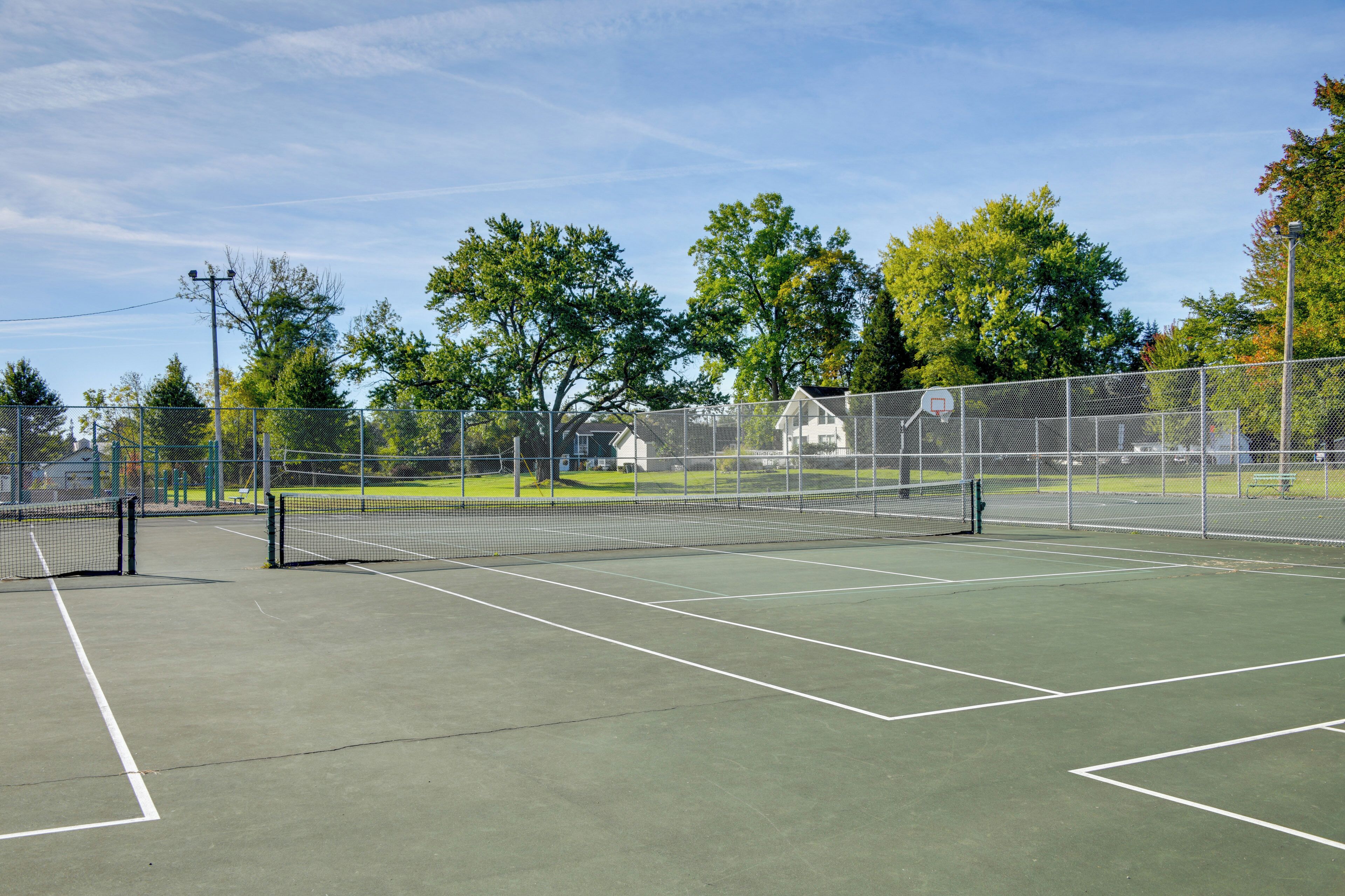 An outdoor tennis court with a net, surrounded by trees and a fence.
