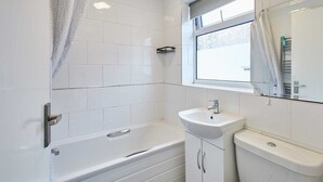 A bathroom with white tiles, a bathtub, a sink, and a toilet.