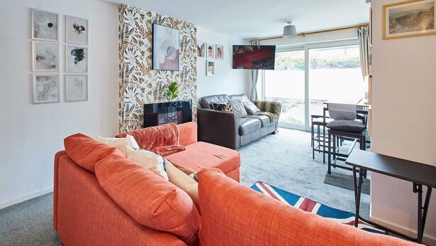 A living room with a sofa, a coffee table, and a TV. There are framed pictures on the wall and a window with curtains.