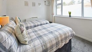 A bedroom with a bed, a radiator, a window with curtains, and a small plant on the windowsill.