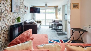 A hotel room with a sofa, a TV, a dining area, and a view of the outdoors.