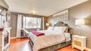 A bedroom with a bed, a nightstand, a chair, a fireplace, and a window with curtains. - Family-friendly Ontario Home in Central Location! (Ontario)