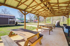 A covered picnic area with wooden benches and picnic tables, surrounded by a grassy lawn and trees.