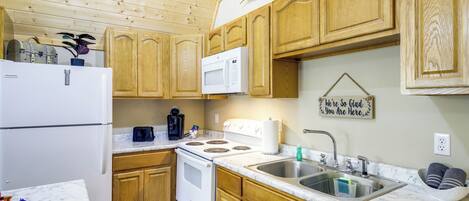 A kitchen with wooden cabinets, a white refrigerator, a microwave, a stove, and a sink.