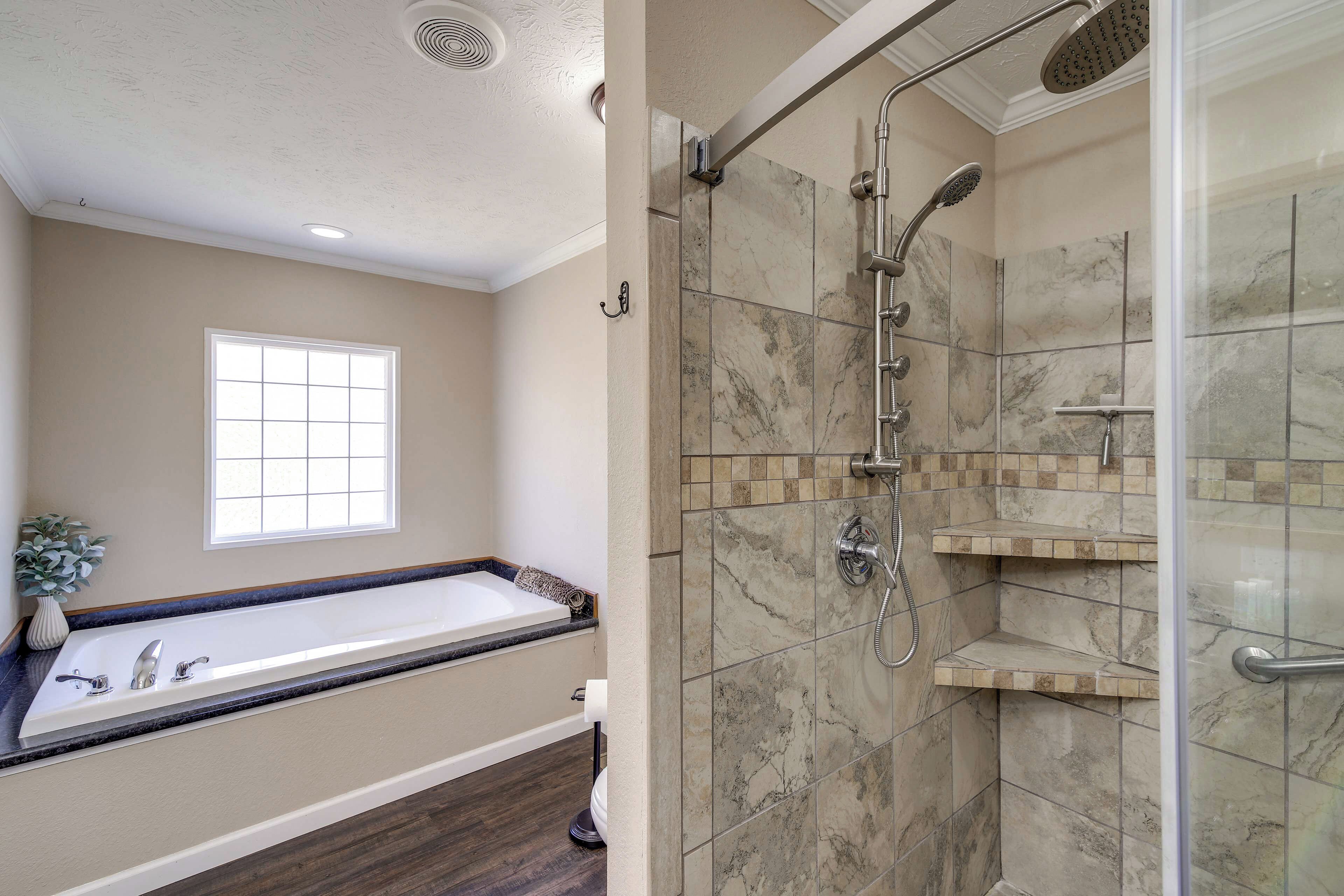 A bathroom with a bathtub, a shower with a glass door, and a window.