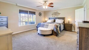 Une chambre à coucher comprenant un lit, une table de chevet, une commode, une fenêtre et un ventilateur de plafond.