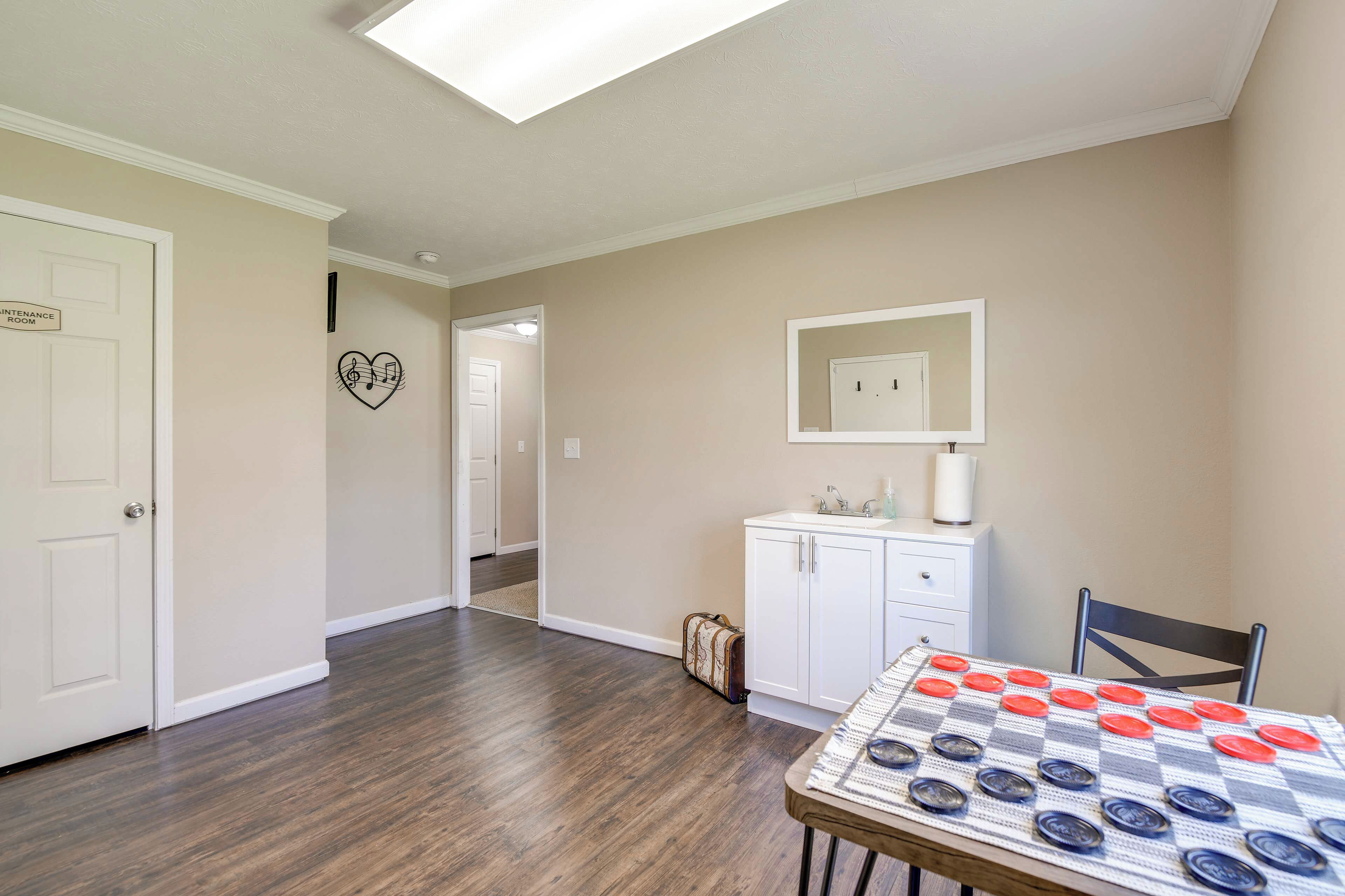 Une pièce avec un plancher en bois, une table à manger recouverte d’une nappe à carreaux, un buffet blanc et un miroir au mur.