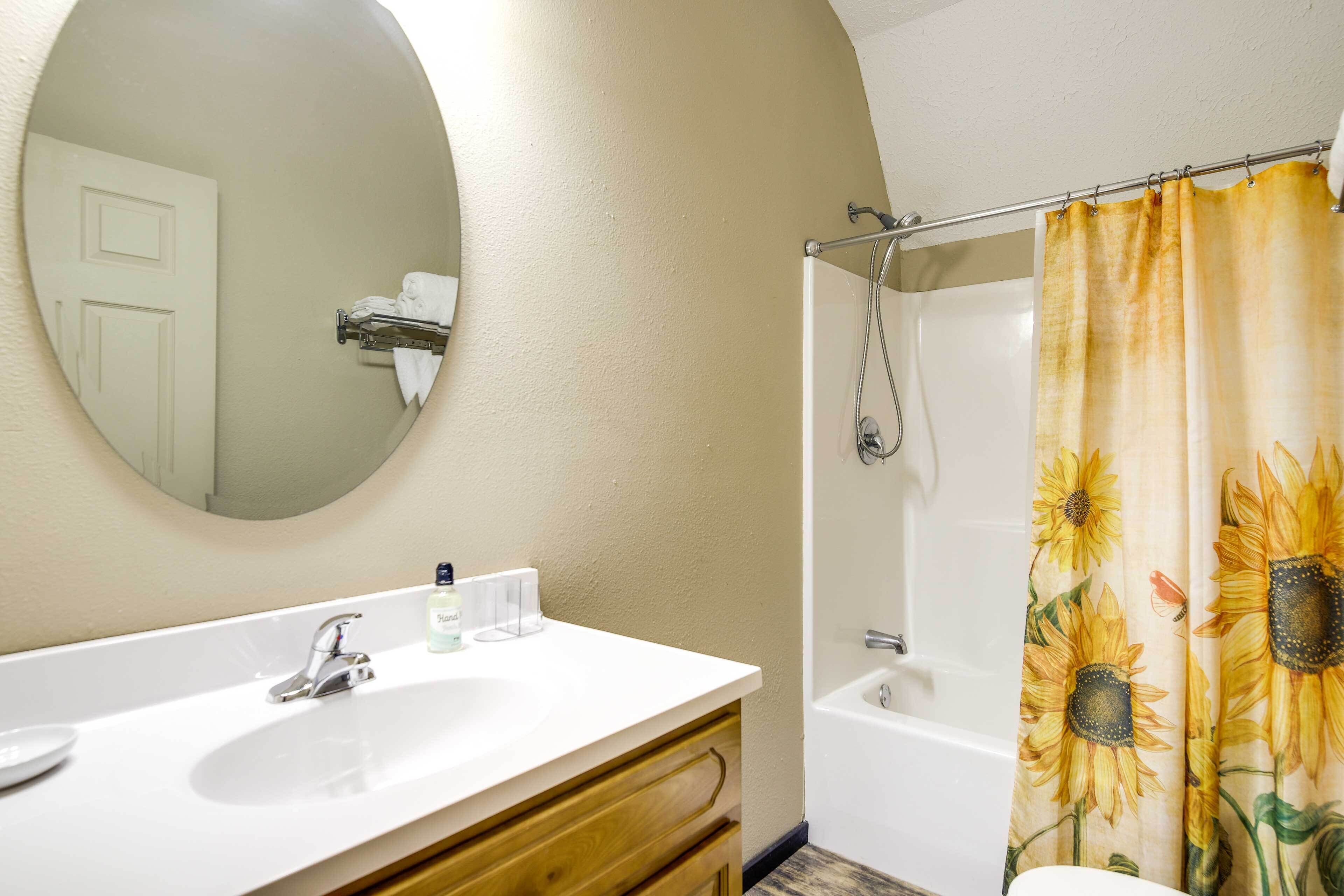 Un baño con lavamanos blanco, espejo y cortina de ducha con diseño de girasoles.