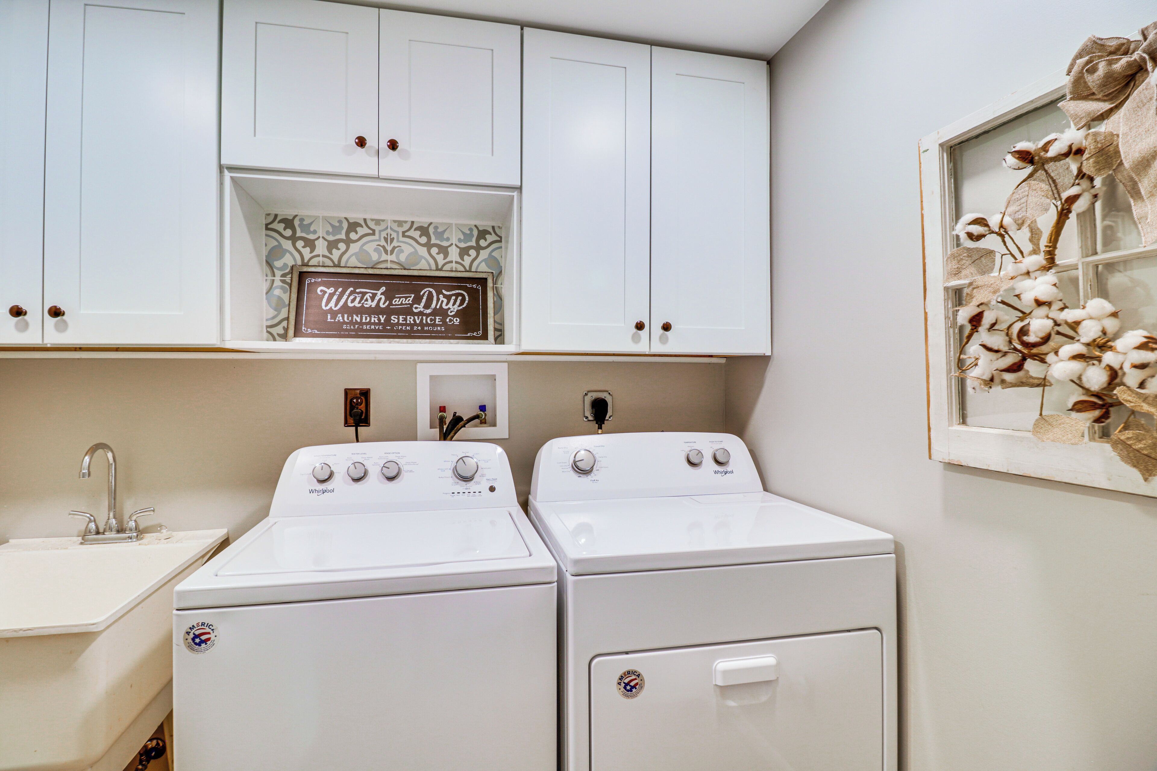 A laundry room with two Whirlpool washers and dryers, a sink, and a sign above the dryers.