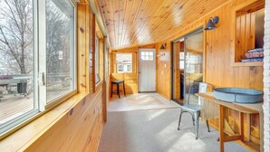 L’intérieur d’un chalet en bois, avec une grande fenêtre, une porte, une petite table et un banc.