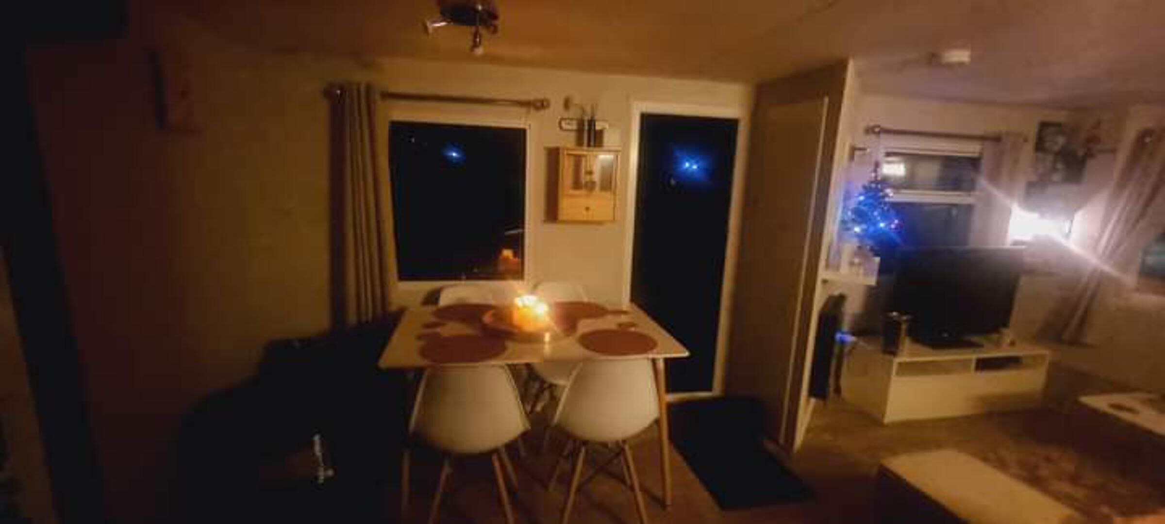 A dining area with a table and chairs, a lit candle, and a view of the night sky through a window.