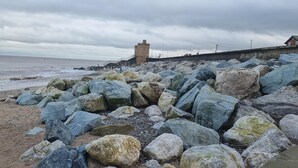 Uma praia rochosa com uma torre e um calçadão à beira-mar.