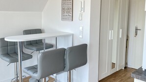 Eine moderne Küche mit weißer Arbeitsplatte, grauen Barhocker und einer hängenden Leuchte.