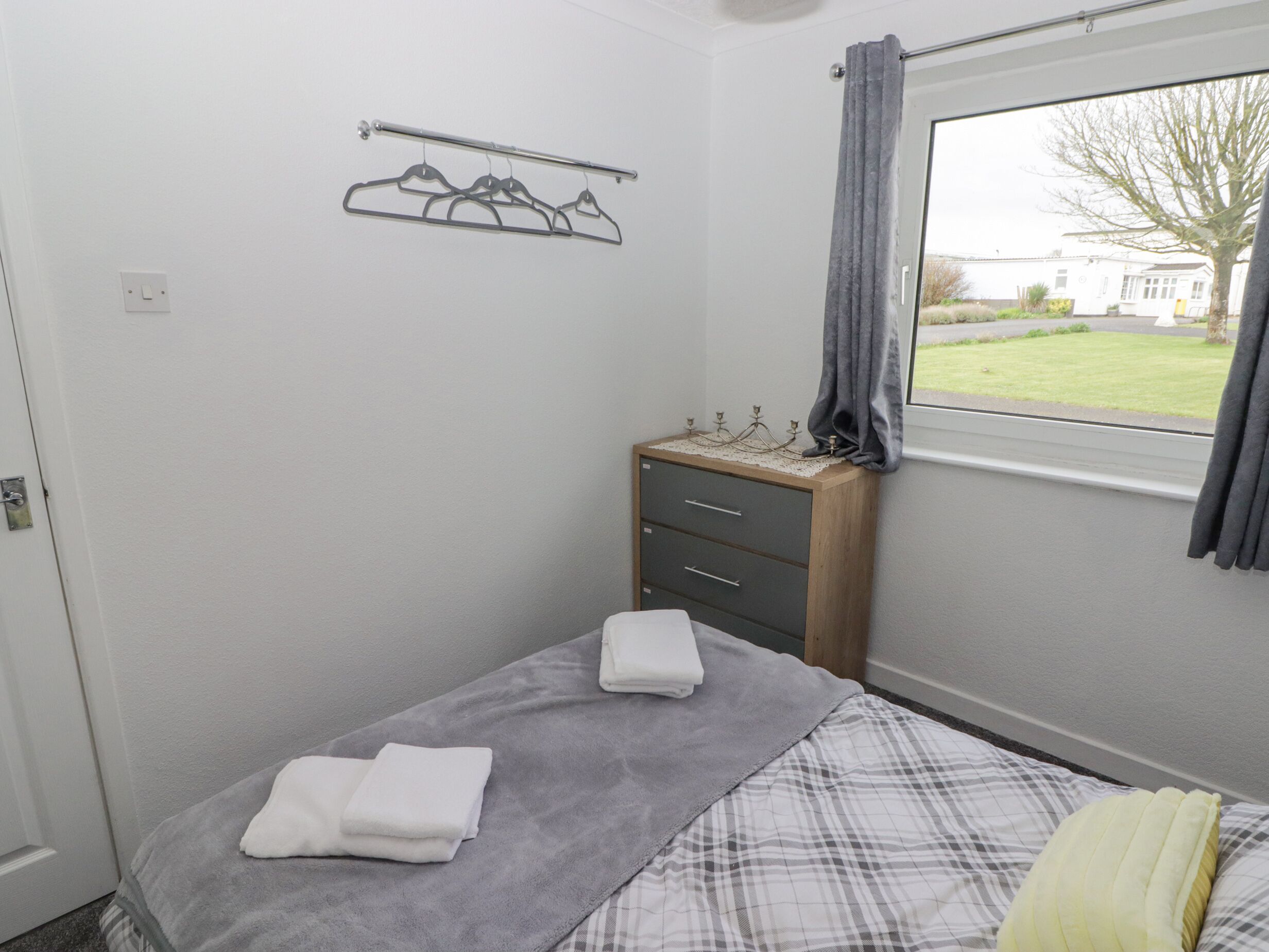 A bedroom with a bed, a dresser, a towel rack, and a window with a view of a house and lawn.