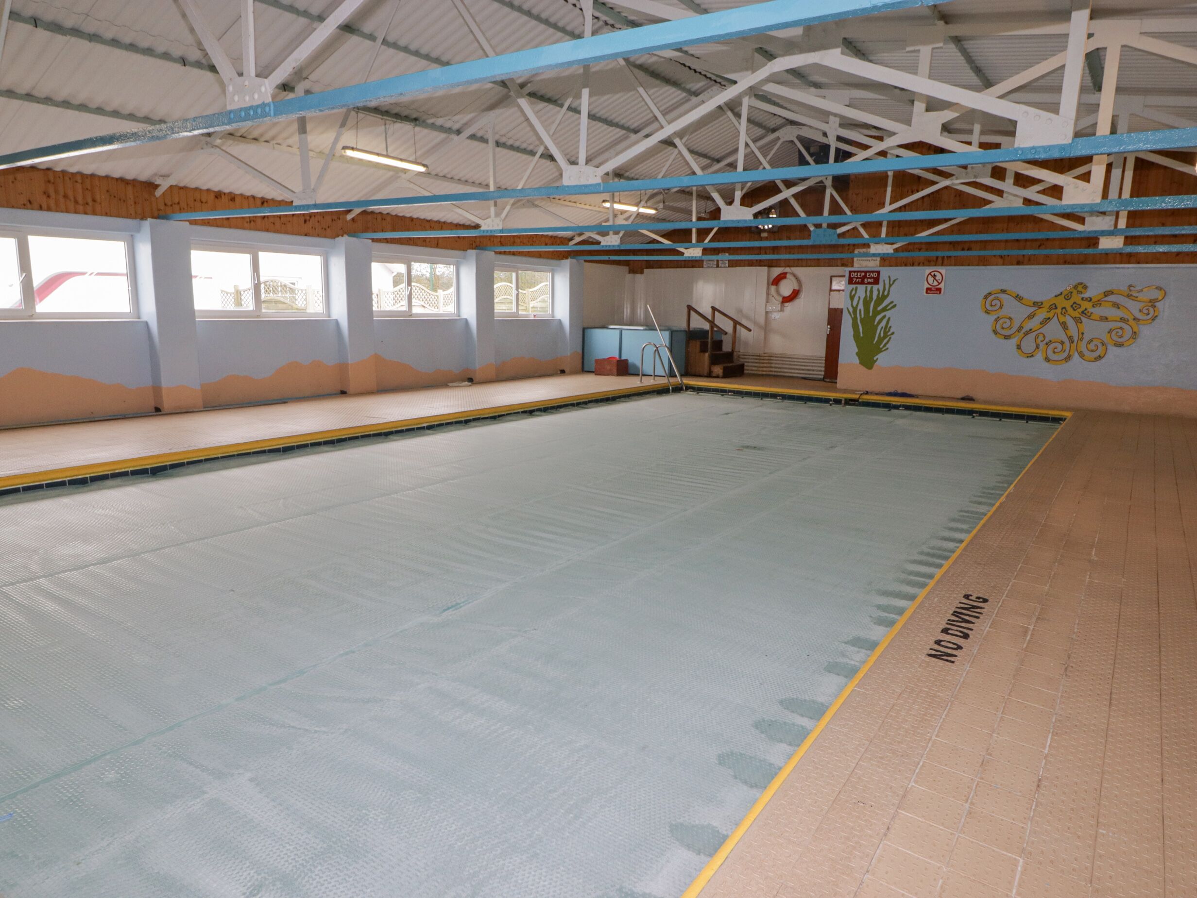 An indoor swimming pool with a diving board, a lifebuoy, and a sign indicating a deep end.