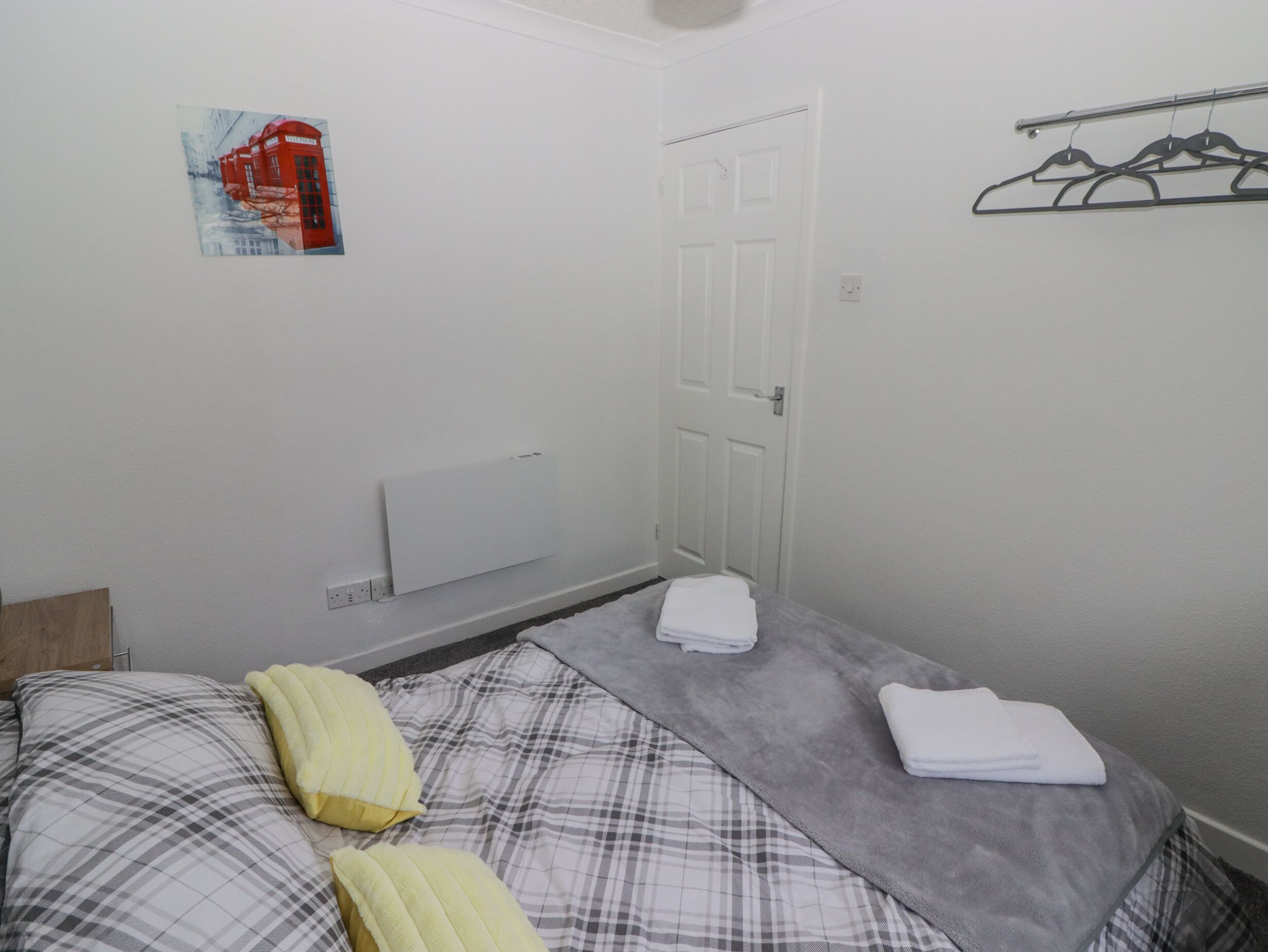 A small, clean room with a bed, a radiator, a door, and a wall-mounted coat rack.