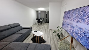 Un soggiorno moderno con un divano grigio, un tavolino da caffè bianco, un quadro appeso alla parete e un'area pranzo sullo sfondo.