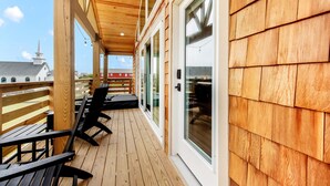 A wooden deck with outdoor seating and large windows overlooking a building with a steeple. - OBX Couples Getaway With Hot Tub-Short Walk to the Beach (Rodanthe)