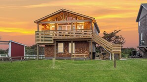 A two-story house with a wooden deck and a staircase leading to the upper level. - OBX Couples Getaway With Hot Tub-Short Walk to the Beach (Rodanthe)