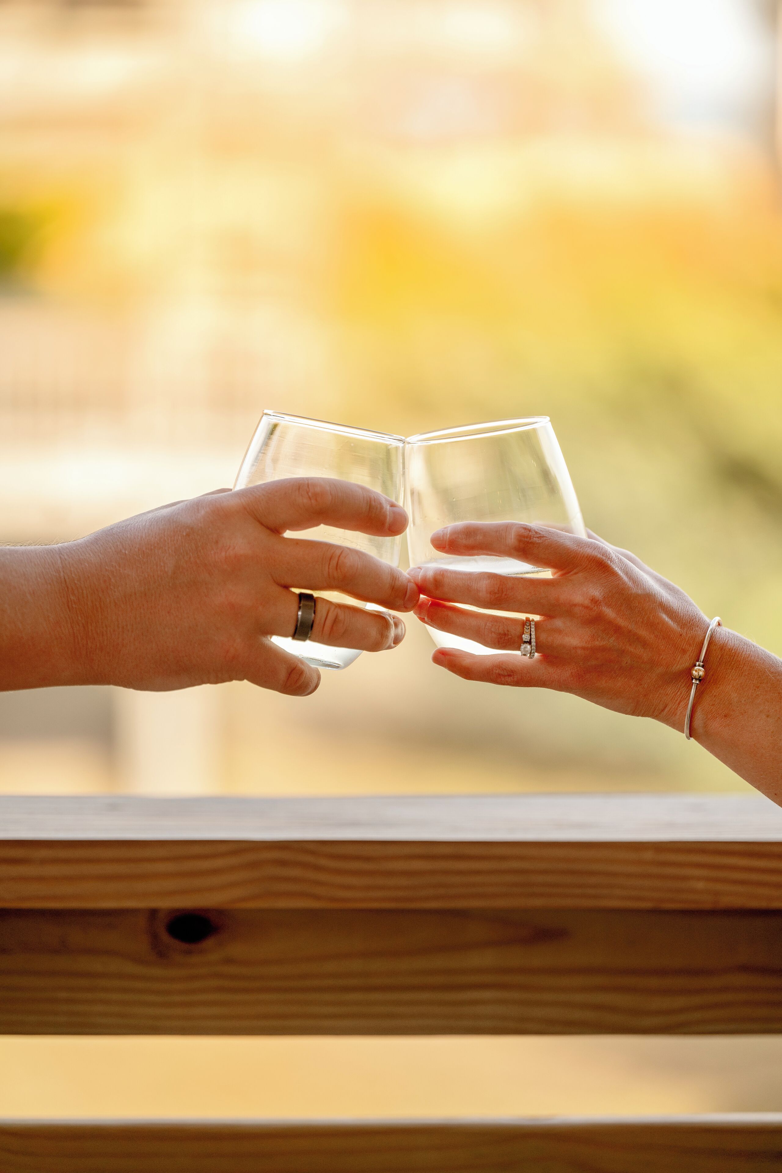 Two hands holding a clear glass, likely containing a beverage, against a blurred background with a wooden surface in the foreground.