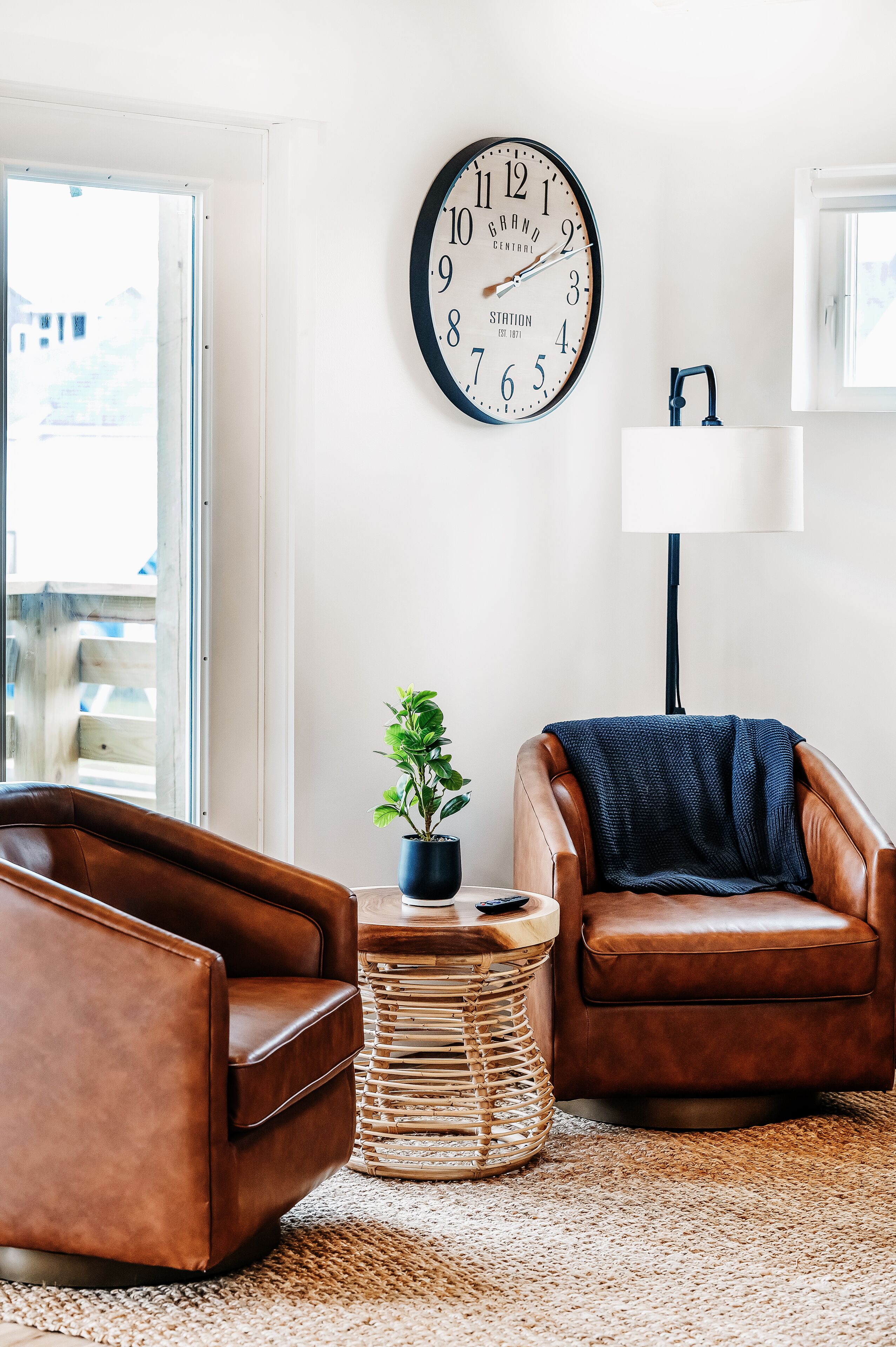 Un salon avec deux fauteuils en cuir marron, une horloge murale ronde, une lampe et une petite plante posée sur une table d’appoint.