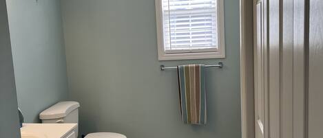 Une salle de bain comprenant des toilettes, un lavabo, une fenêtre avec des stores et un porte-serviettes.
