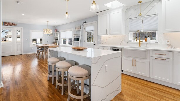 Una cocina moderna con armarios blancos, una isla de mármol y taburetes de madera.