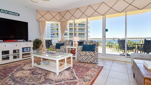 Ein geräumiges Wohnzimmer mit großem Flachbildfernseher, Couchtisch, gemusterten Sofas und Meerblick.