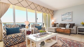 Ein Wohnzimmer mit einem gemusterten Sofa, einem Glastisch und einem großen Fenster mit Blick.