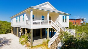Ein zweistöckiges Strandhaus mit Balkon und einer Treppe, die zum Obergeschoss führt.